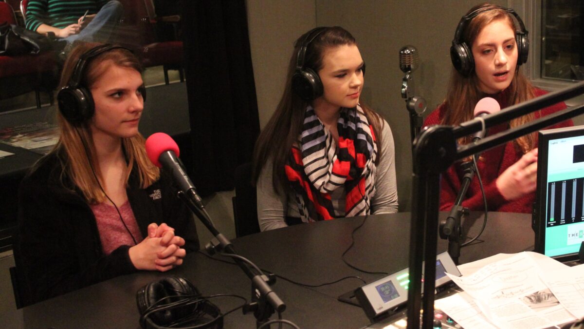 Three teens wearing headphones speaking into microphones in a radio studio