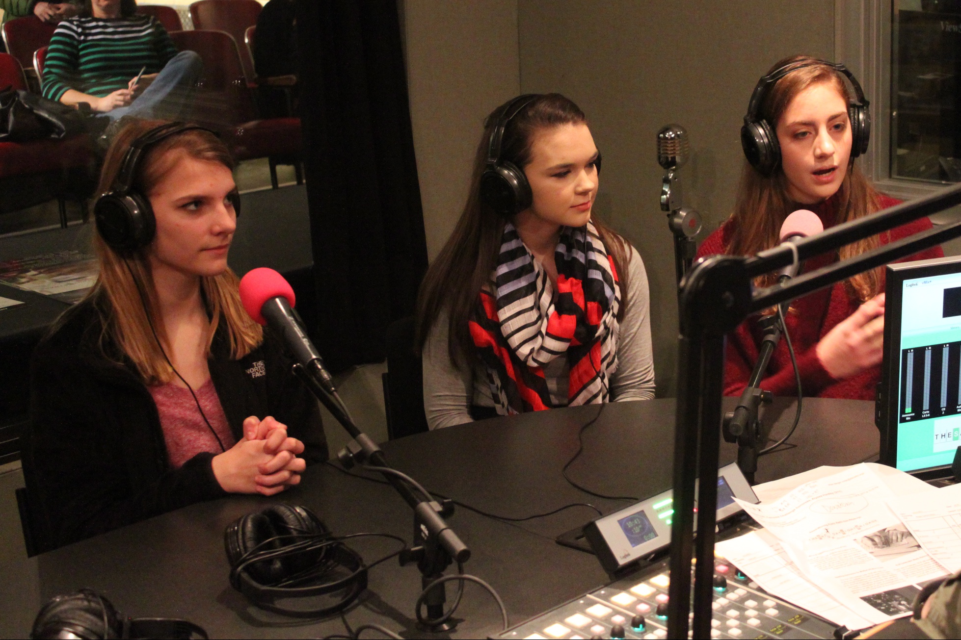 Three teens wearing headphones speaking into microphones in a radio studio