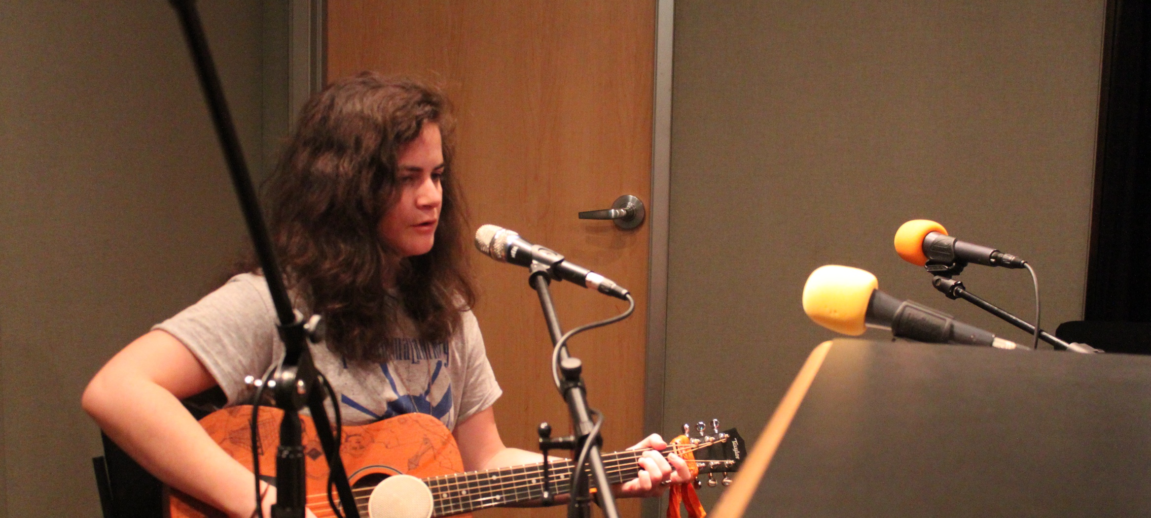 An adult playing an acoustic guitar and singing into a microphone in a radio studio