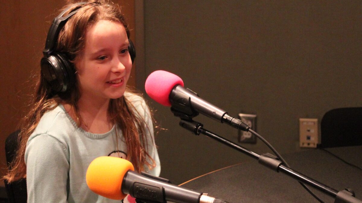 A youth wearing headphones speaking into a microphone in a radio studio