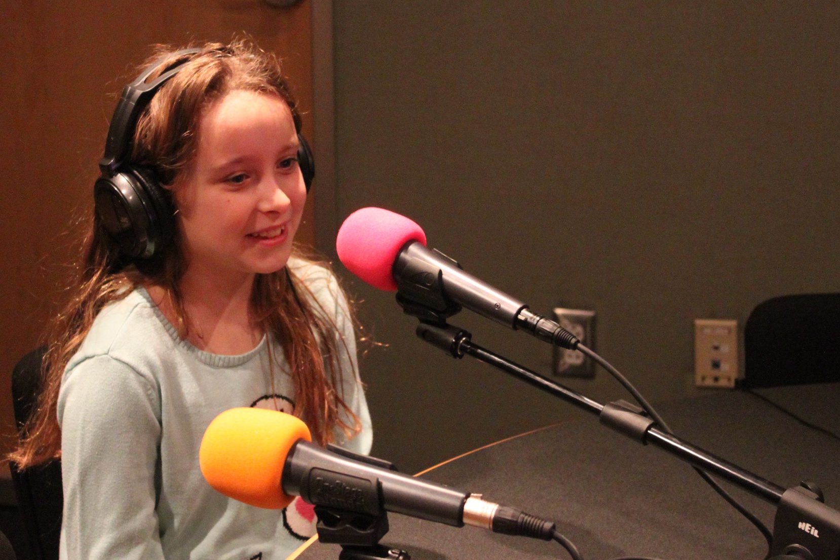 A youth wearing headphones speaking into a microphone in a radio studio
