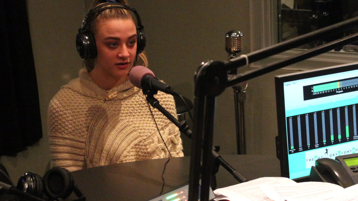 A teen wearing headphones speaking into a microphone in a radio studio