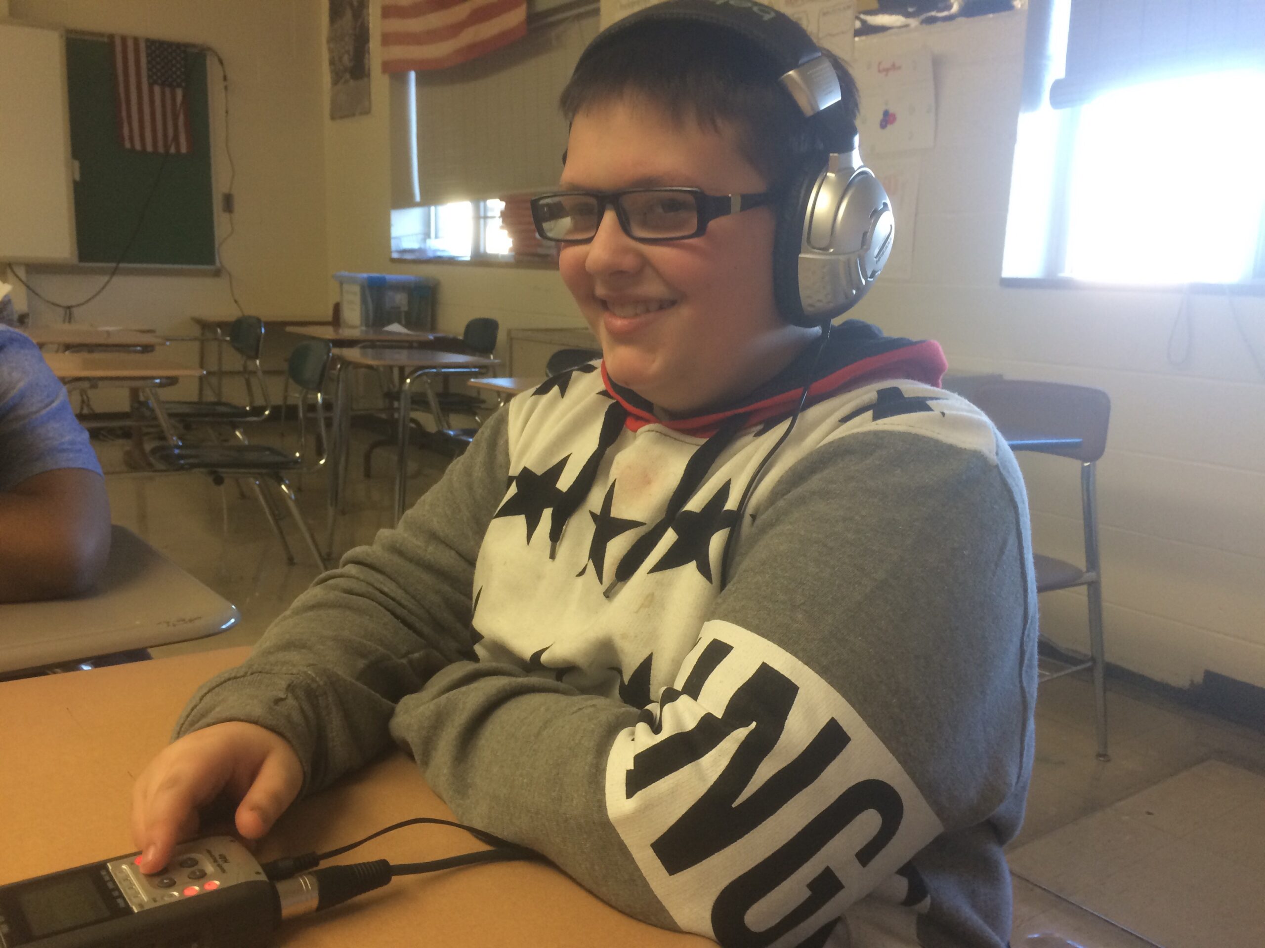 A youth wearing headphones interacting with a portable recorder in a classroom