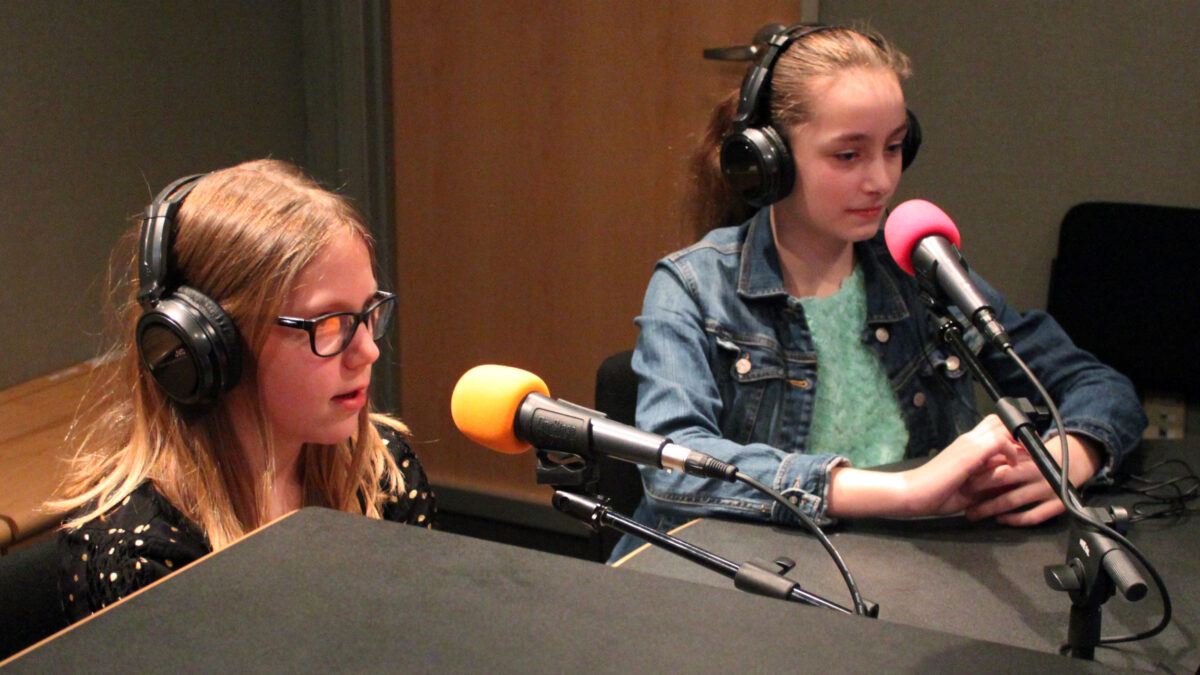 Two youth wearing headphones speaking into microphones in a radio studio