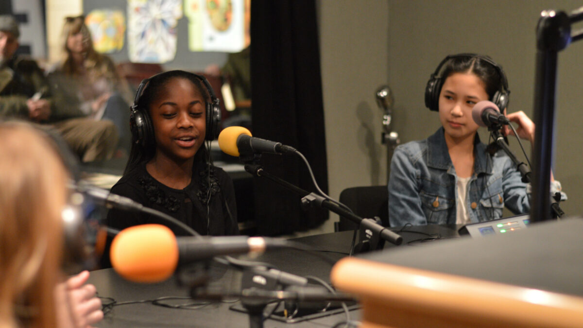 Three youth wearing headphones speaking into microphones in a radio studio