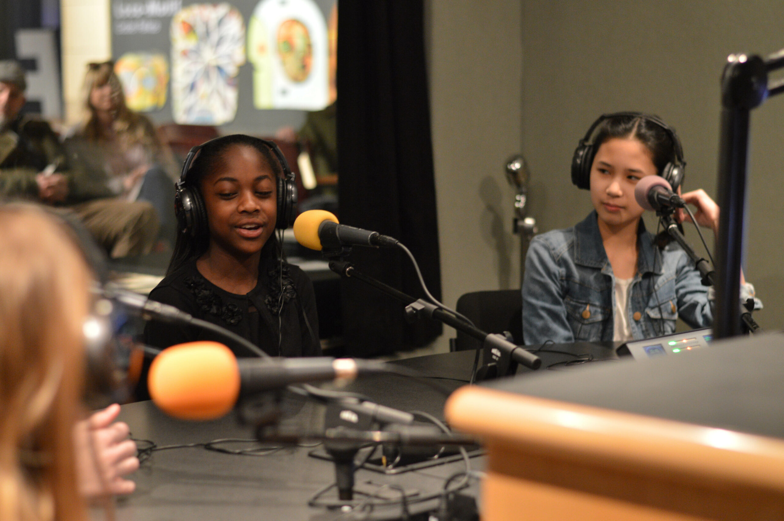 Three youth wearing headphones speaking into microphones in a radio studio