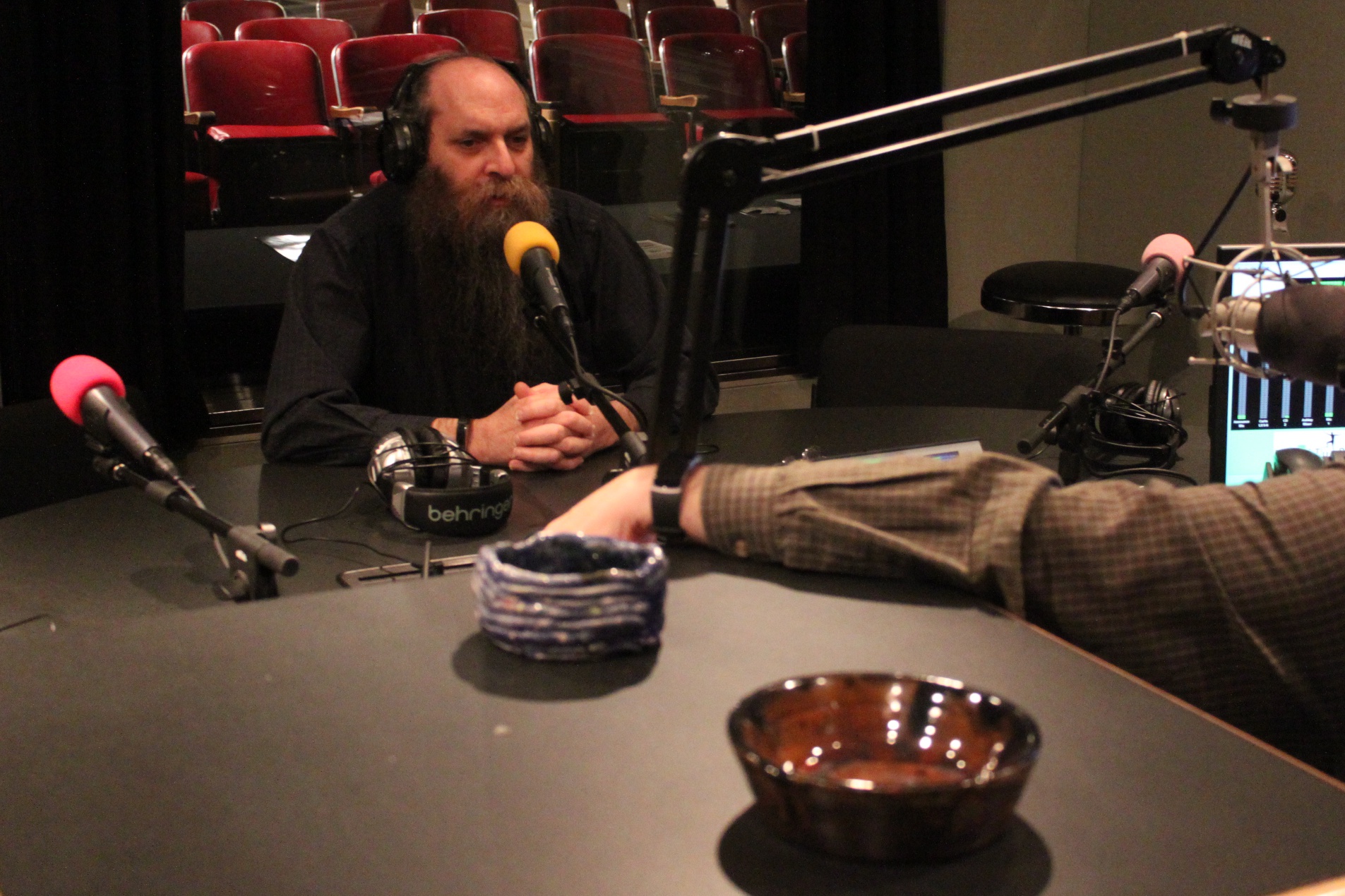 An adult wearing headphones speaking into a microphone being interviewed in a radio studio