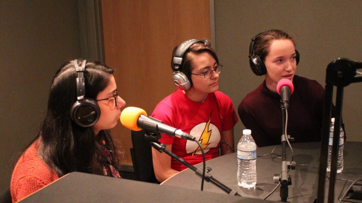 Three teens wearing headphones speaking into microphones in a radio studio