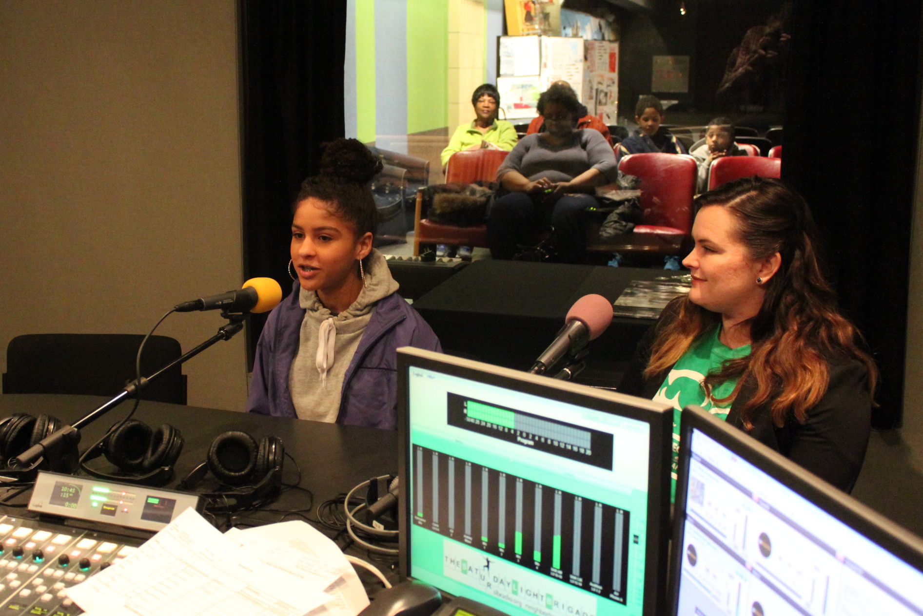 Two teens speaking into headphones in a radio studio