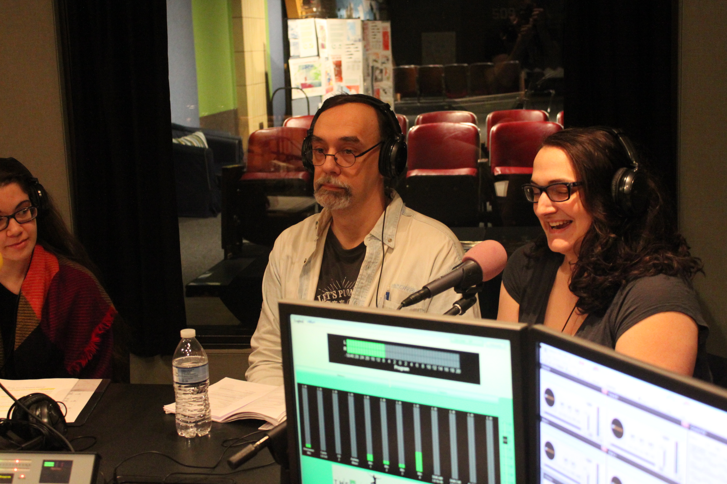 Three adults wearing headphones speaking into microphones in a radio studio