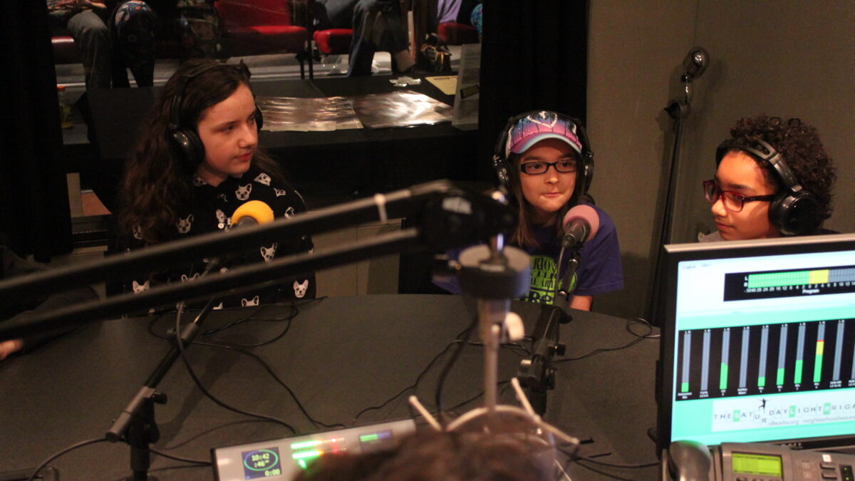 IMG_3227 Three youth wearing headphones speaking into microphones being interviewed in a radio studio