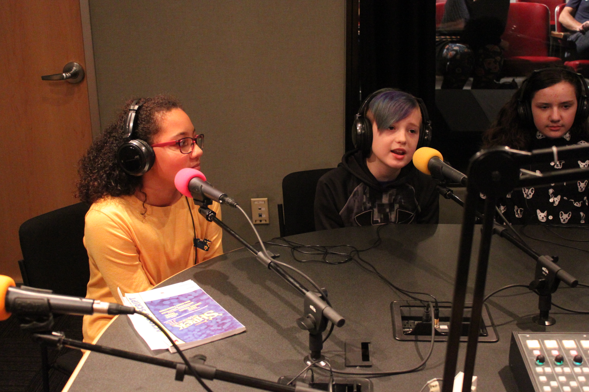 Three youth wearing headphones speaking into microphones in a radio studio