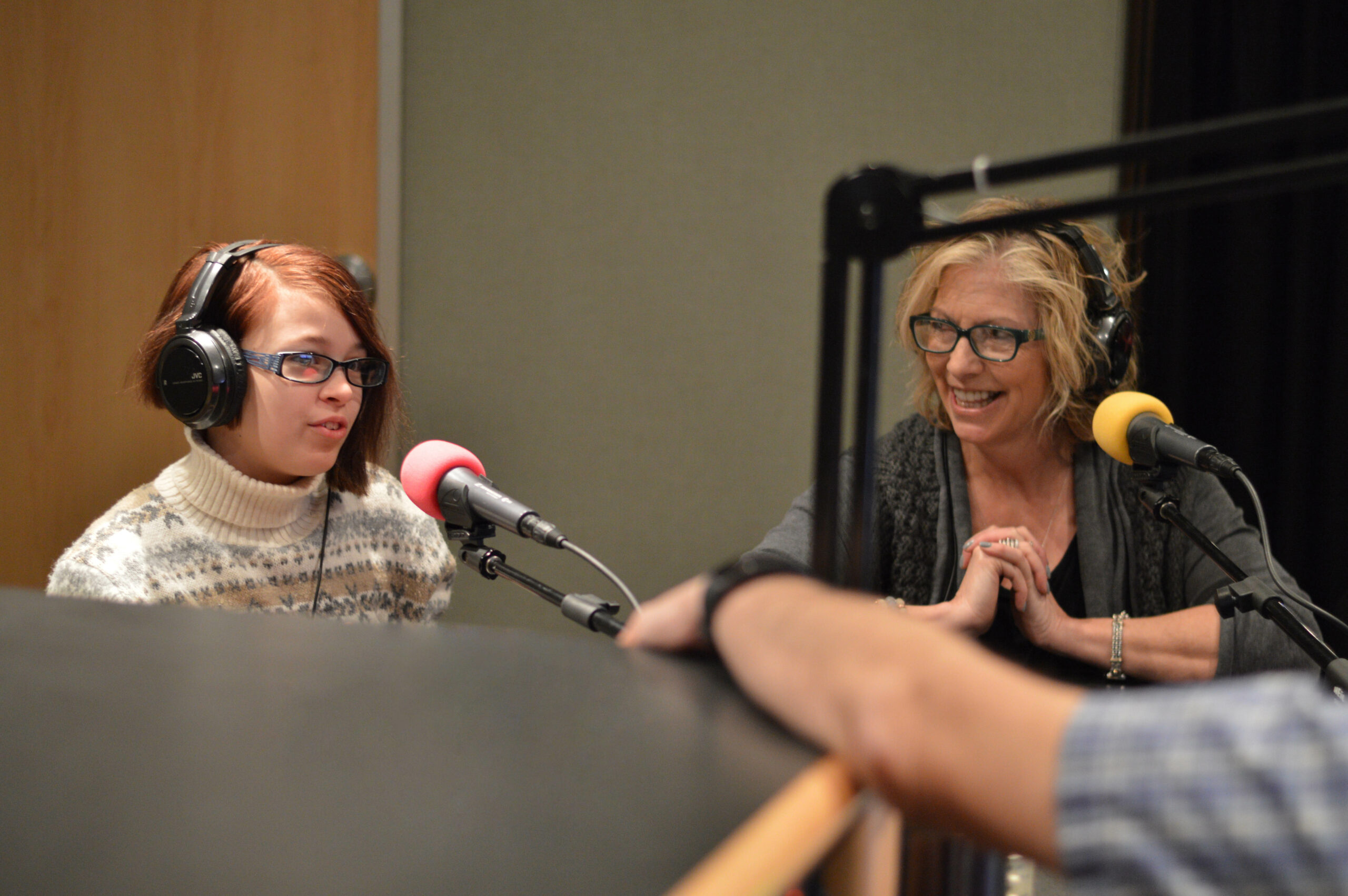 Two individuals wearing headphones speaking into microphones being interviewed in a radio studio