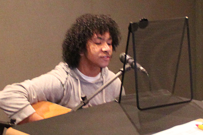 A teen playing acoustic guitar and singing into a microphone in a radio studio