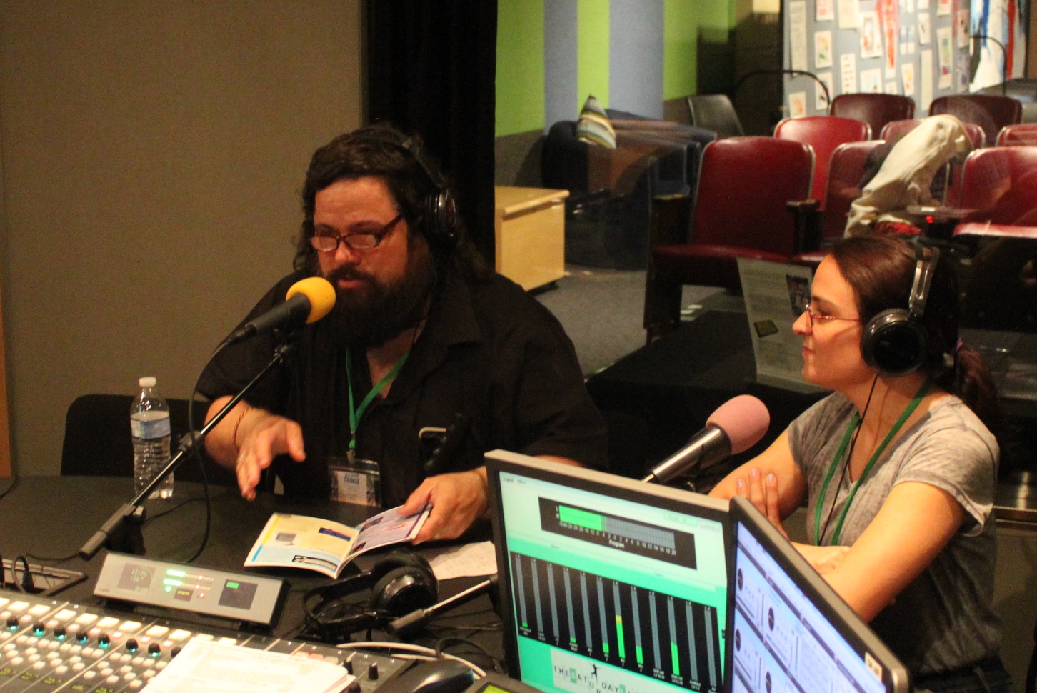 Two adults wearing headphones speaking into microphones in a radio studio