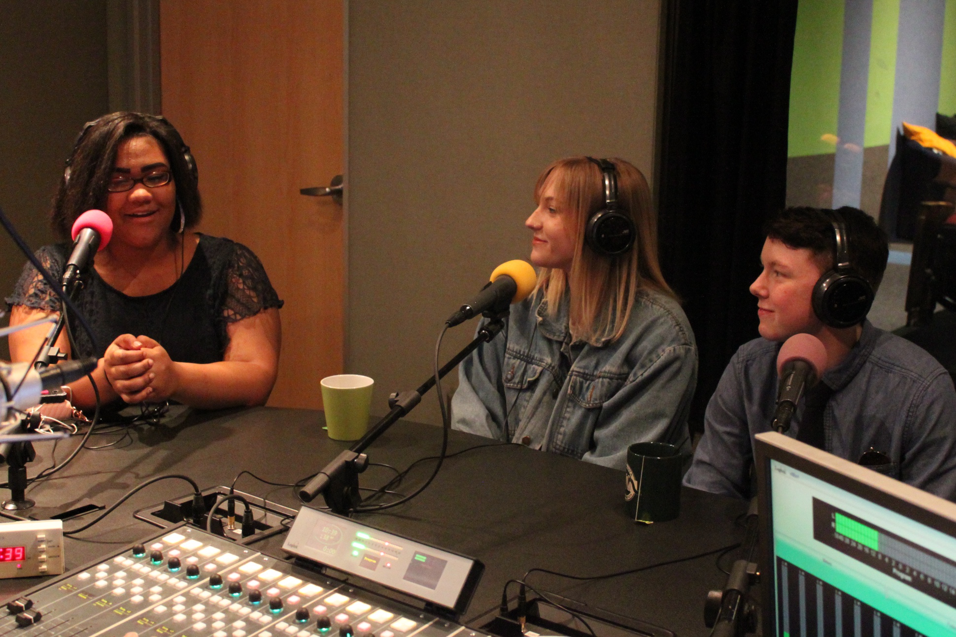 Three teens wearing headphones speaking into microphones in a radio studio