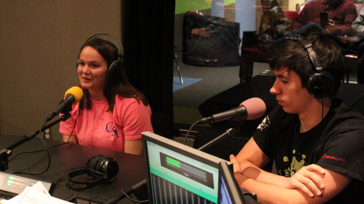 Two teens wearing headphones speaking into microphones in a radio studio