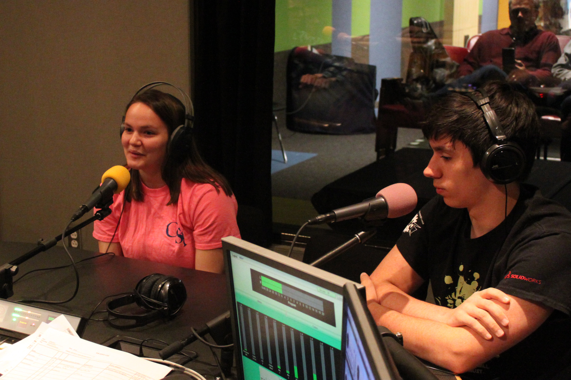 Two teens wearing headphones speaking into microphones in a radio studio