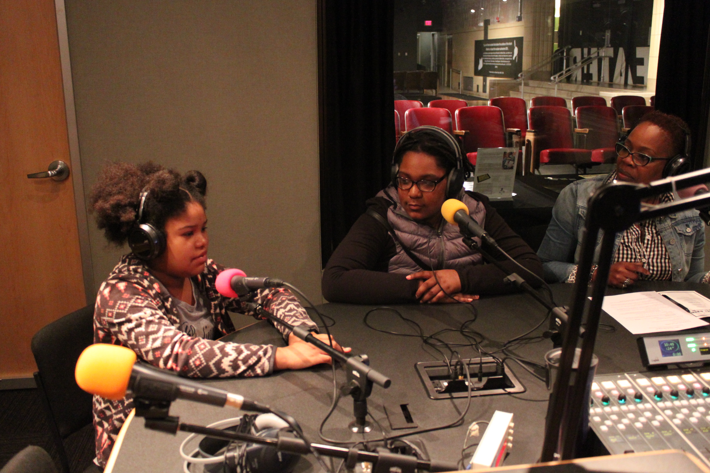 Two youth and an adult wearing headphones speaking into microphones in a radio studio