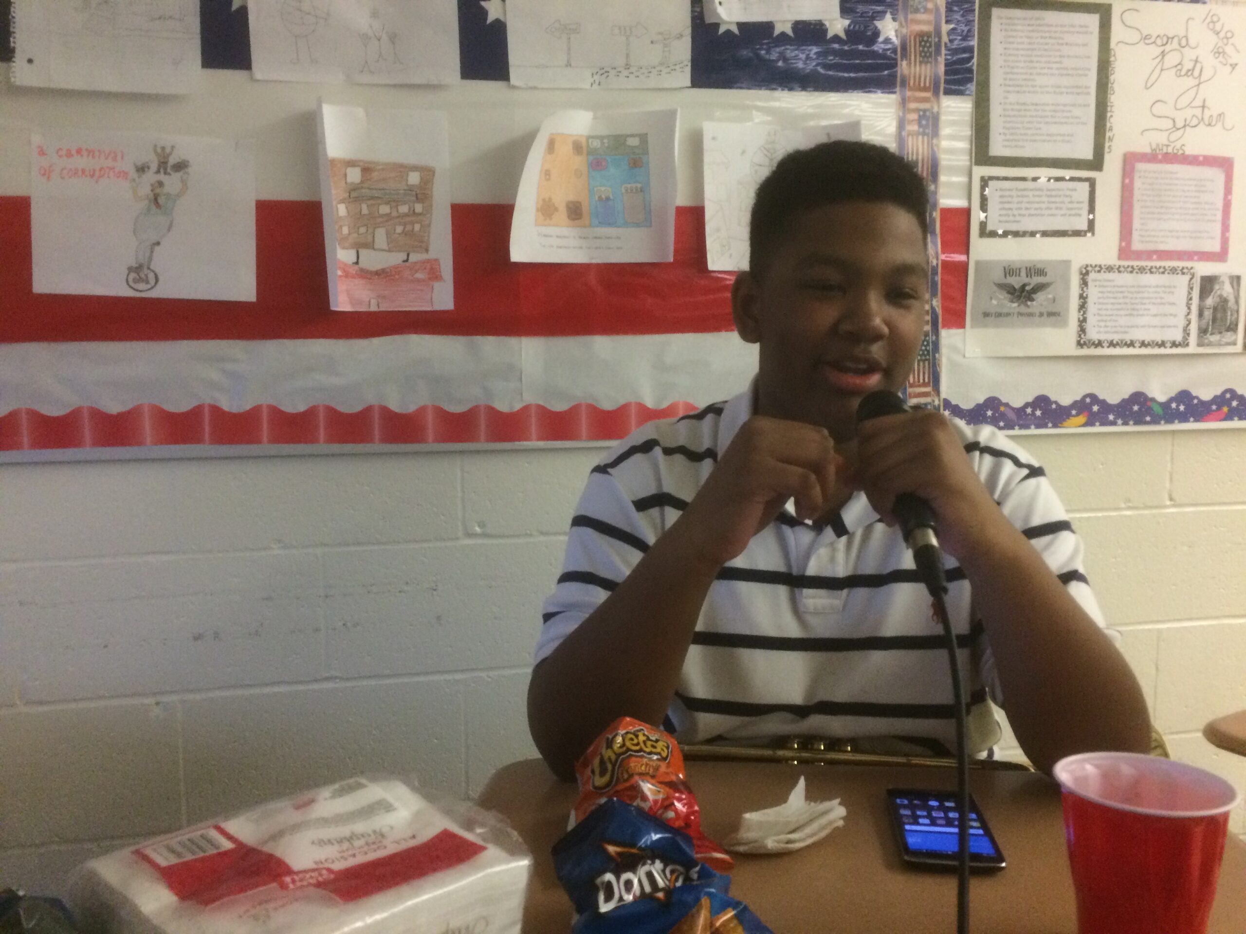 A youth sitting in a classroom speaking into a microphone