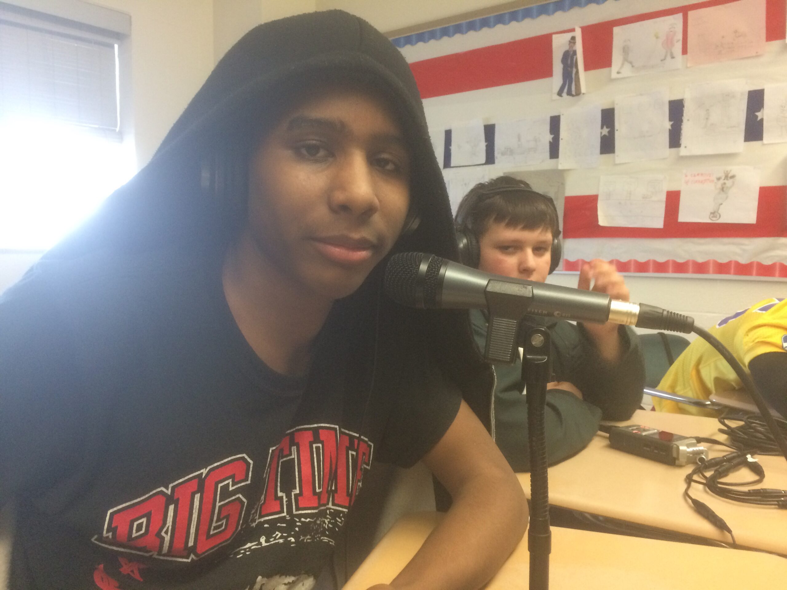 Two youth sitting in a classroom, one speaking into a microphone