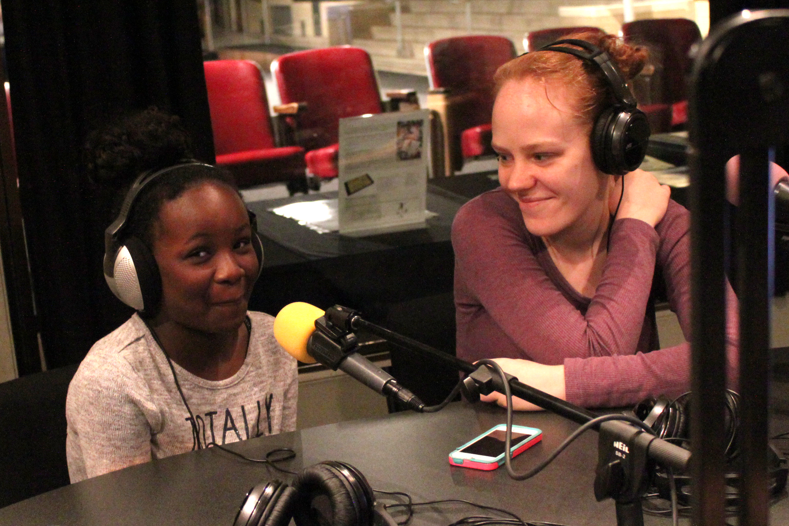 A youth and an adult wearing headphones speaking into microphones in a radio studio