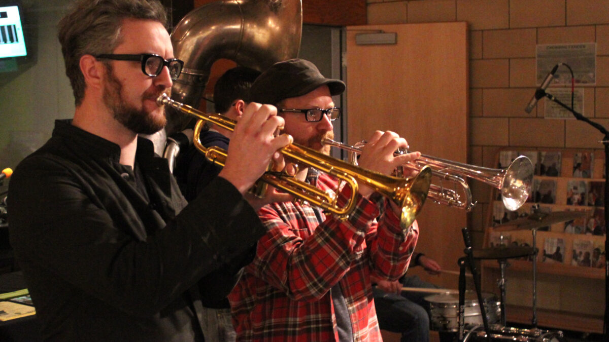 Two adults playing trumpet and an adult playing sousaphone