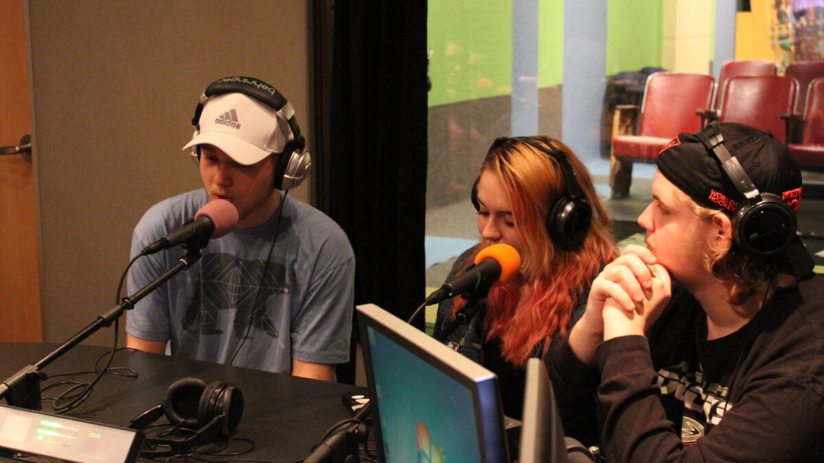 Three teens wearing headphones speaking into microphones in a radio studio