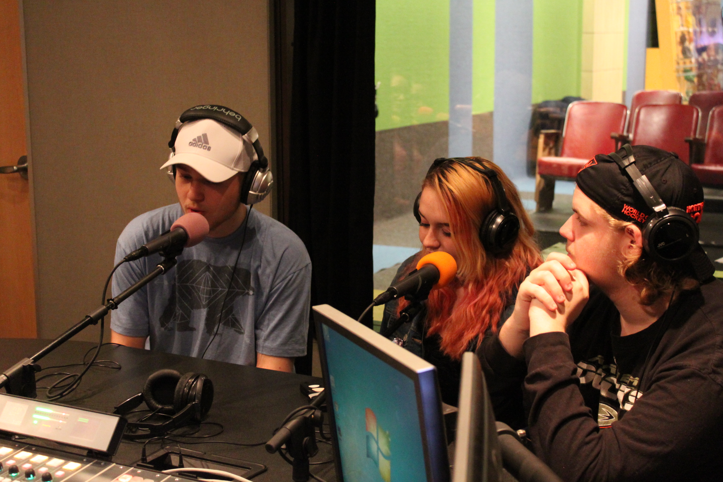 Three teens wearing headphones speaking into microphones in a radio studio