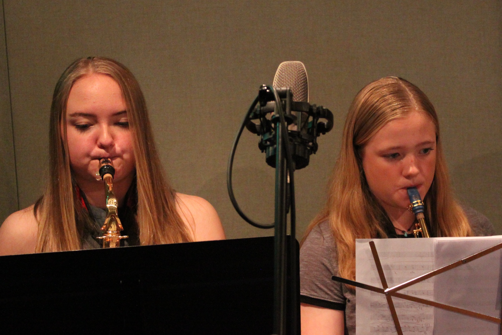 Two teens playing alto saxophones looking at sheet music on music stands in a radio studio
