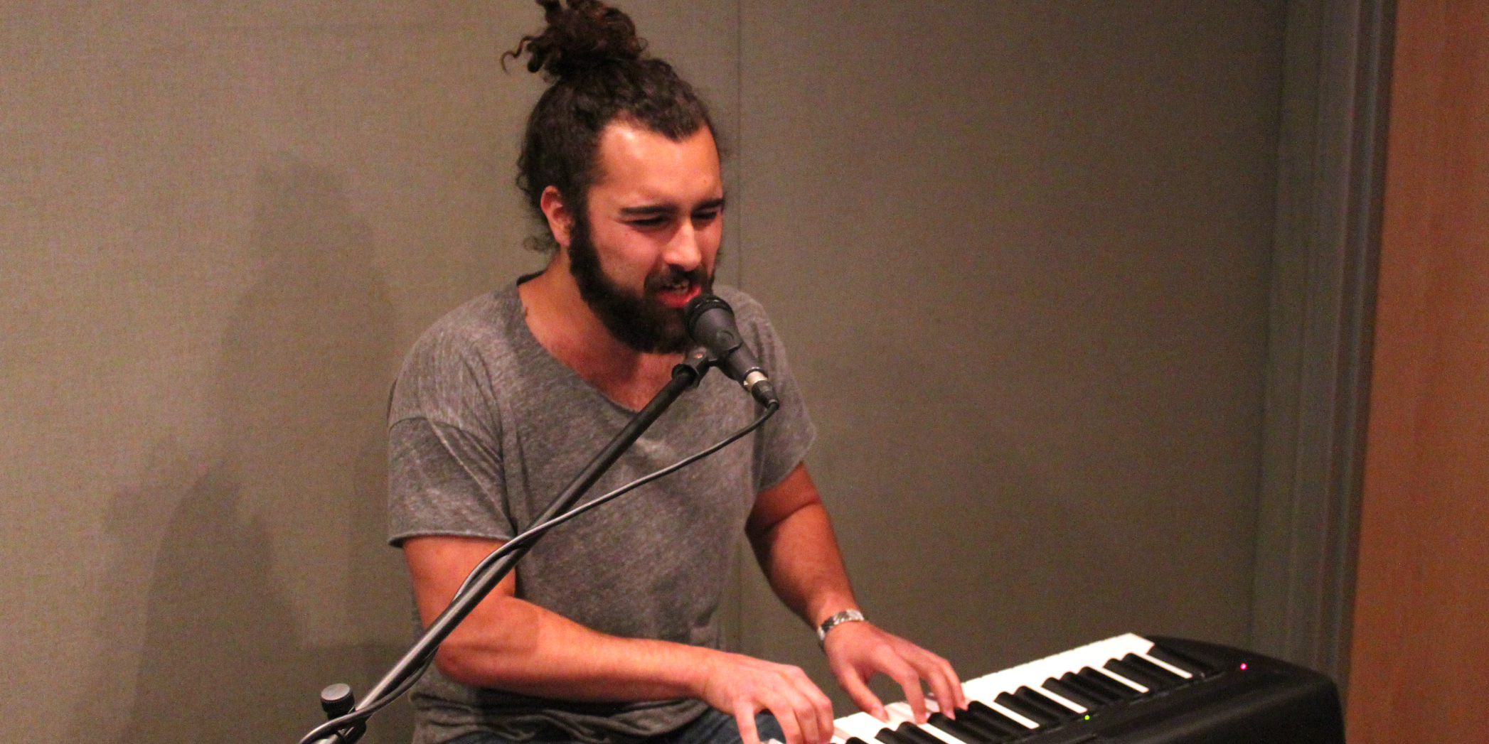 An adult playing a piano keyboard and singing into a microphone in a radio studio