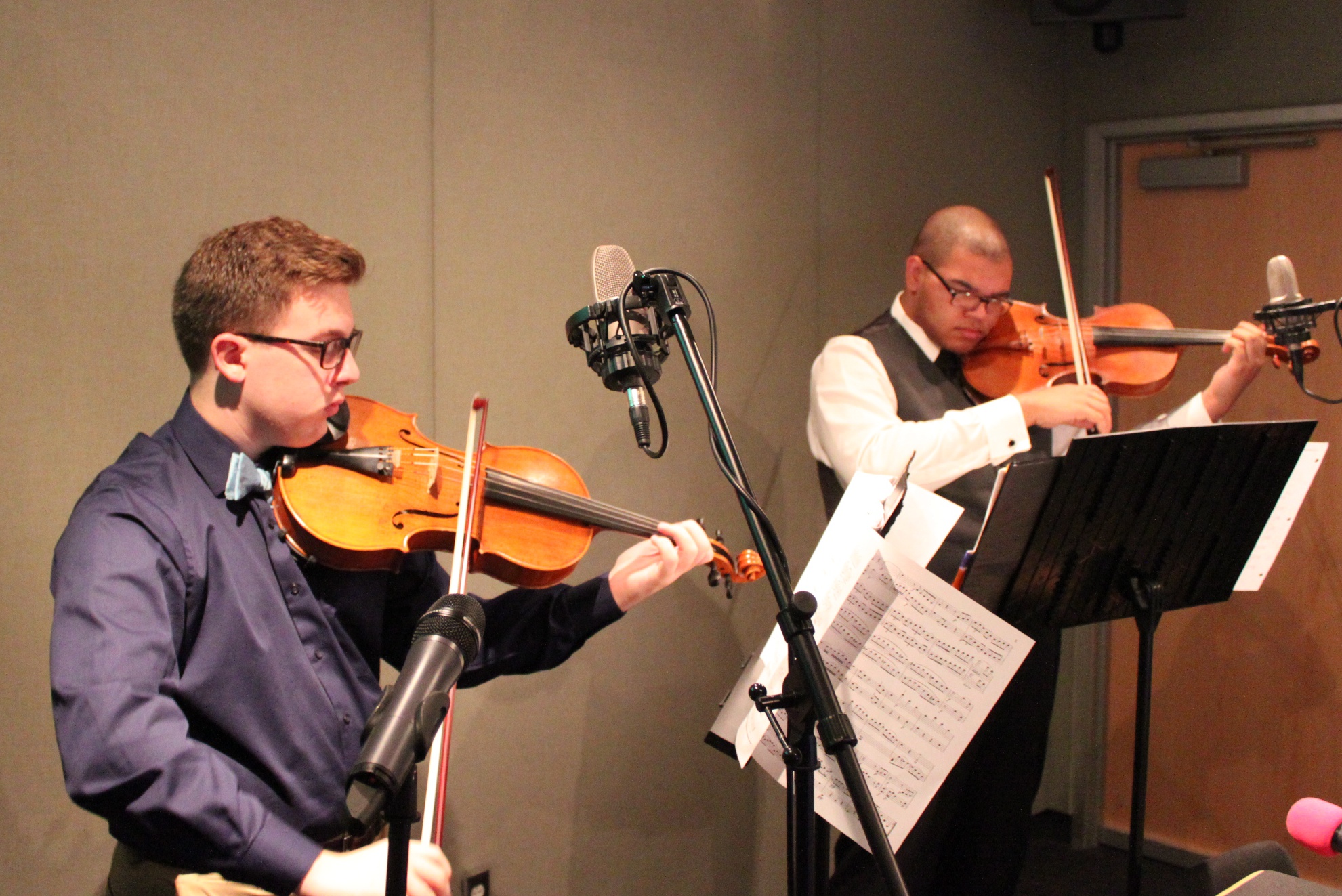 Two teens playing viola looking at sheet music on music stands in a radio studio