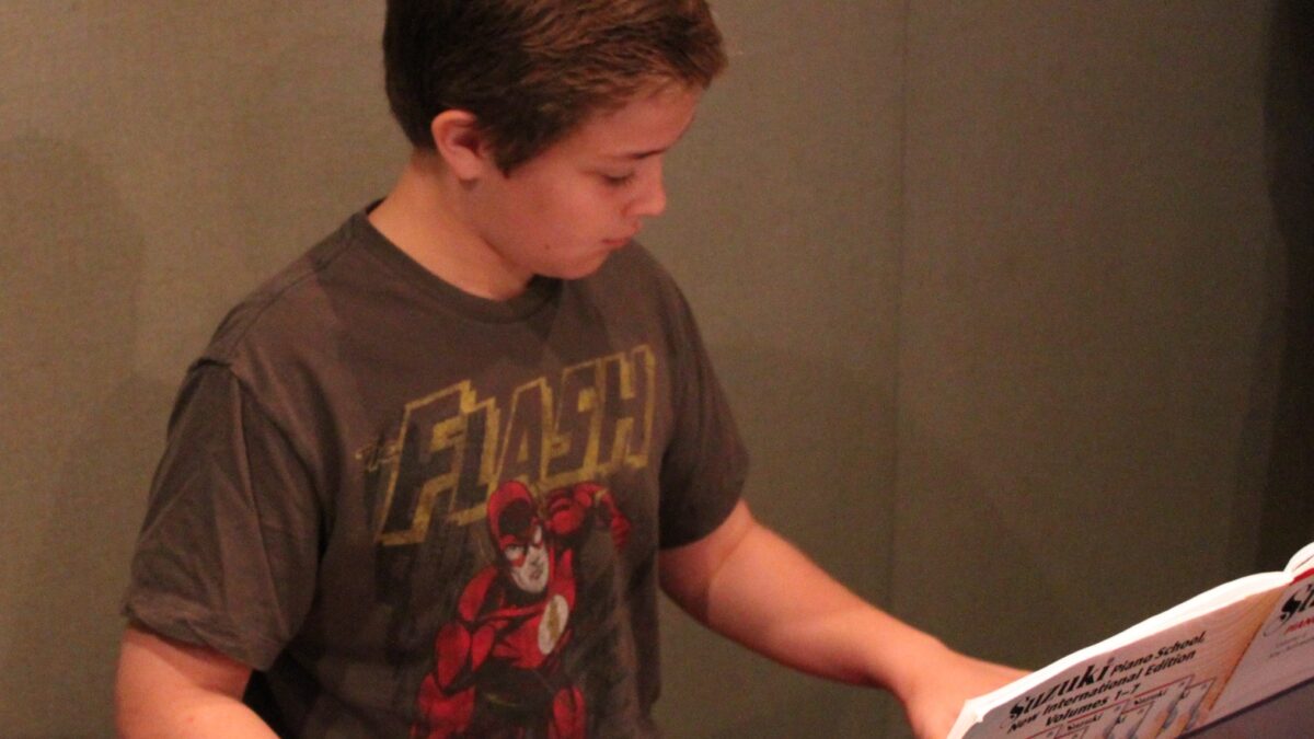 A youth playing a piano keyboard looking at sheet music in a radio studio