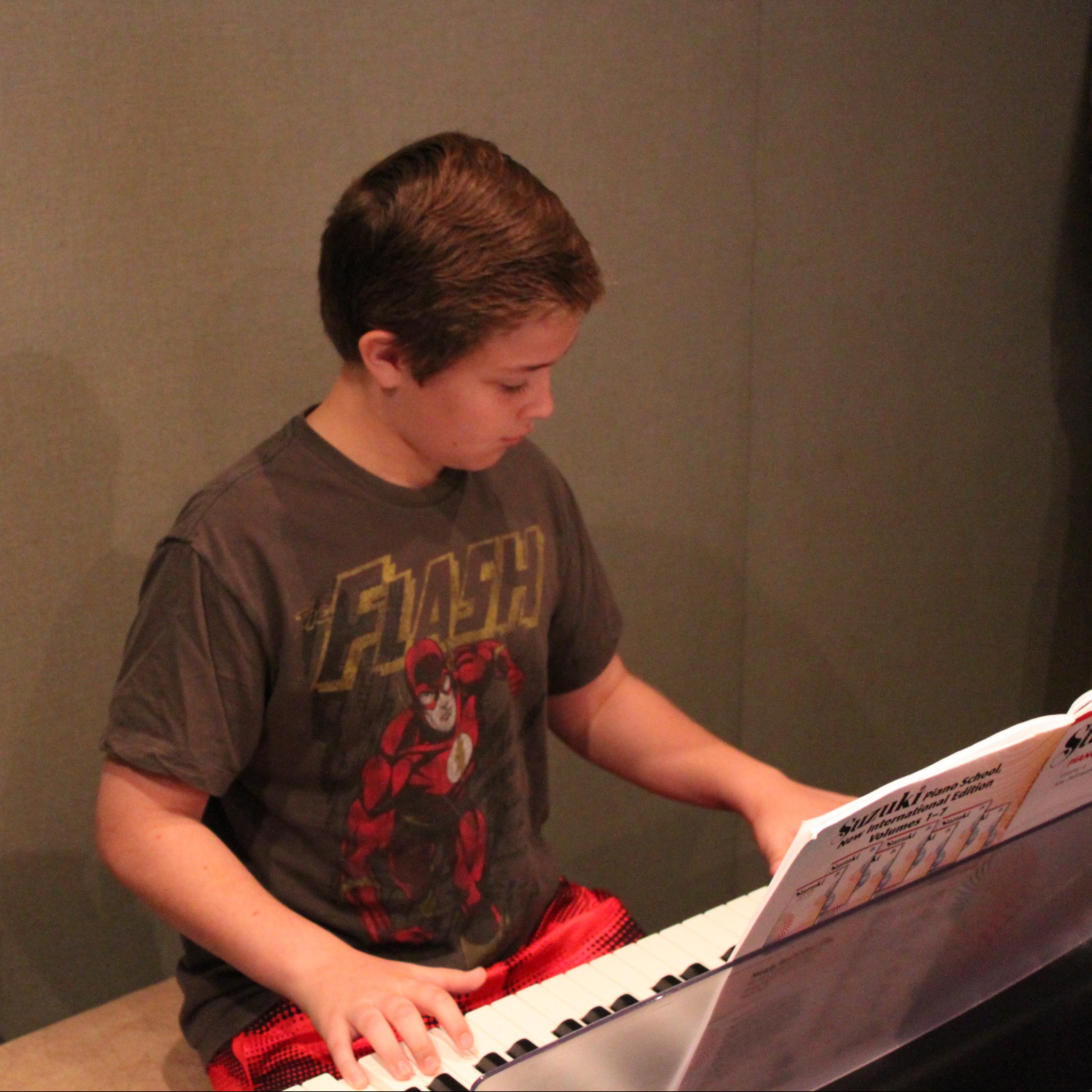 A youth playing a piano keyboard looking at sheet music in a radio studio