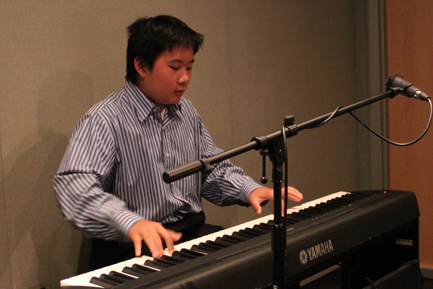 A teen playing a piano keyboard sitting behind a microphone in a radio studio