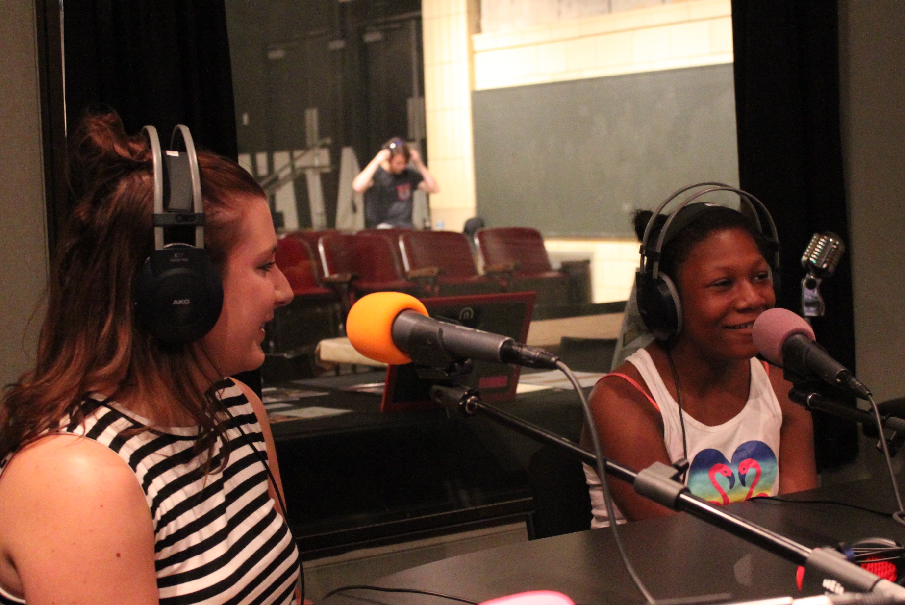 An adult and a youth wearing headphones speaking into microphones in a radio studio
