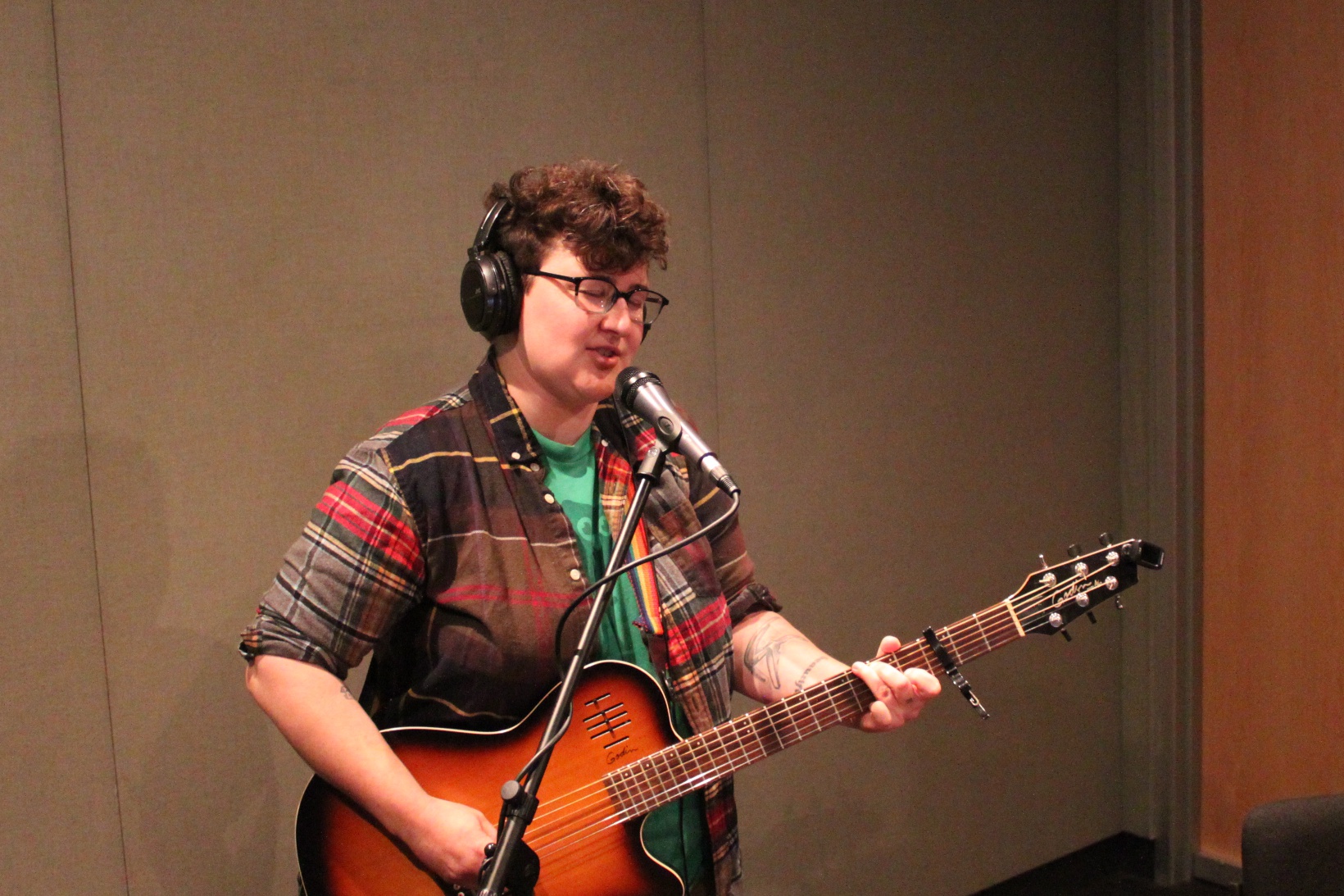 An adult playing an acoustic guitar and singing into a microphone in a radio studio
