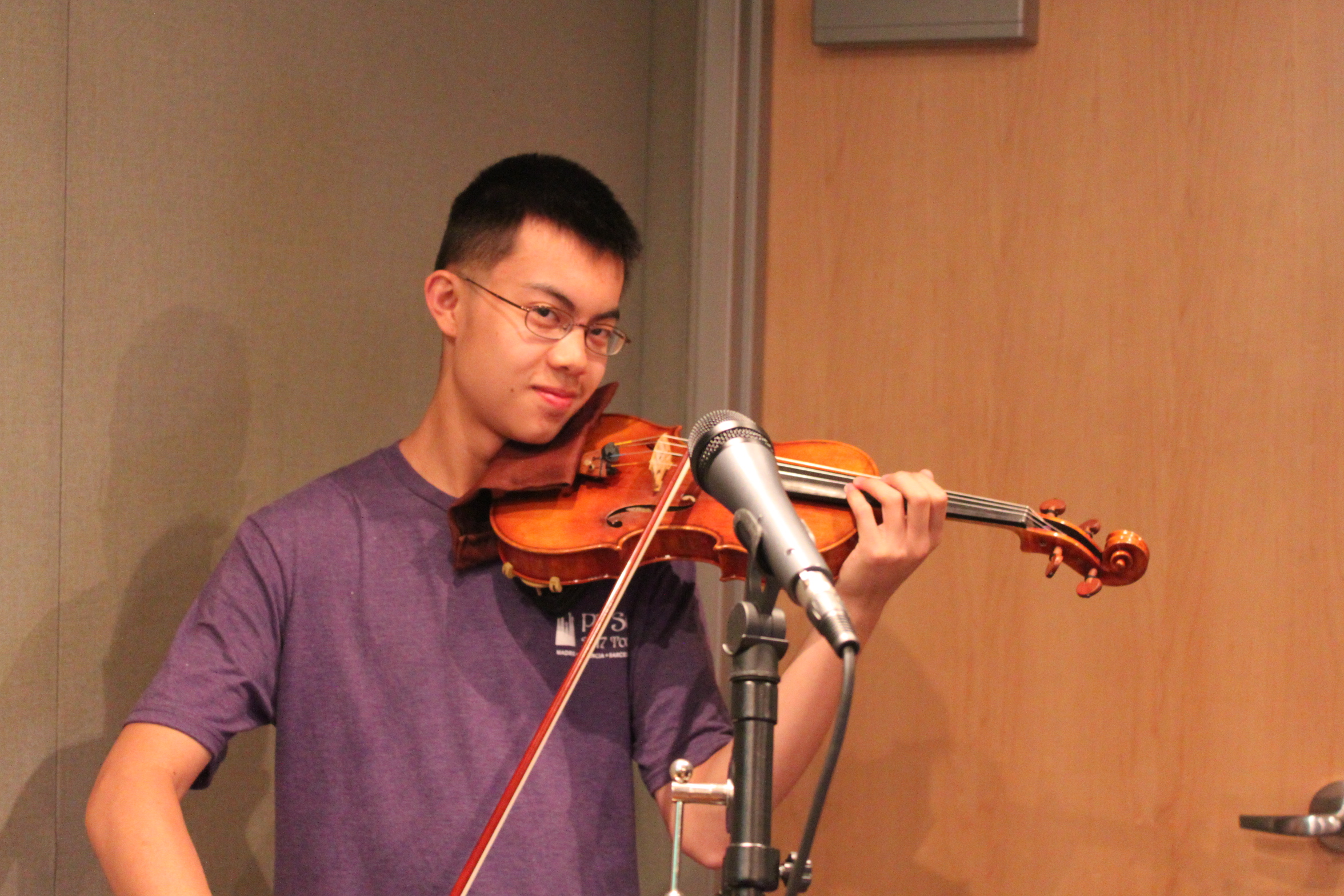 A teen playing violin into a microphone in a radio studio
