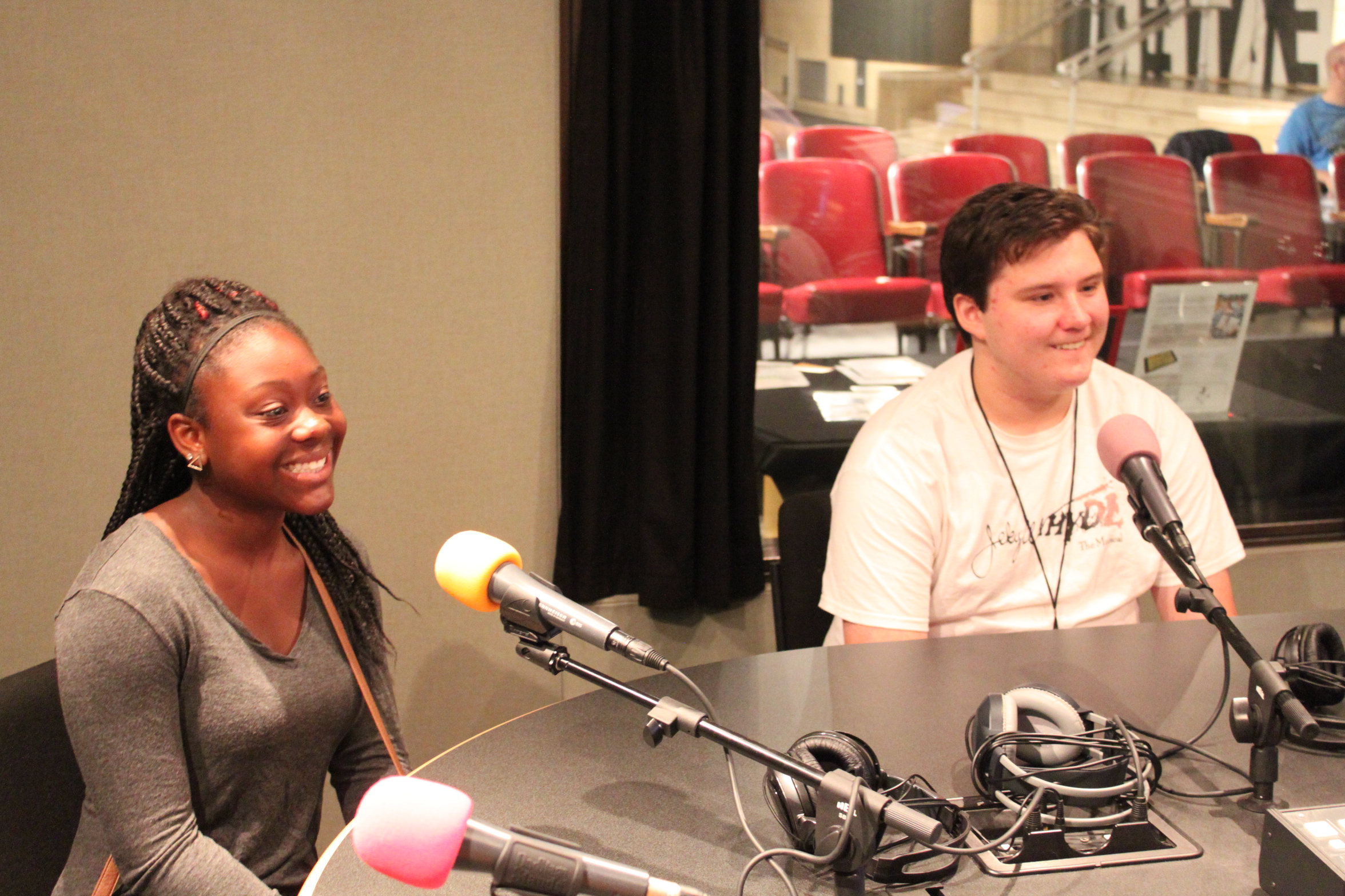 Two teens smiling behind microphones in a radio studio