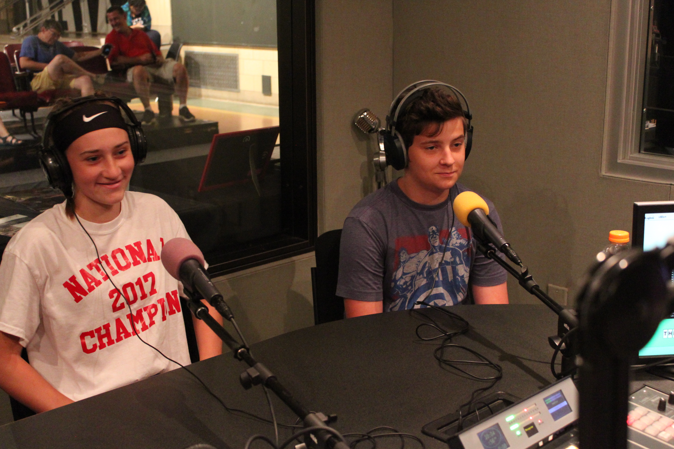 Two teens wearing headphones speaking into microphones in a radio studio