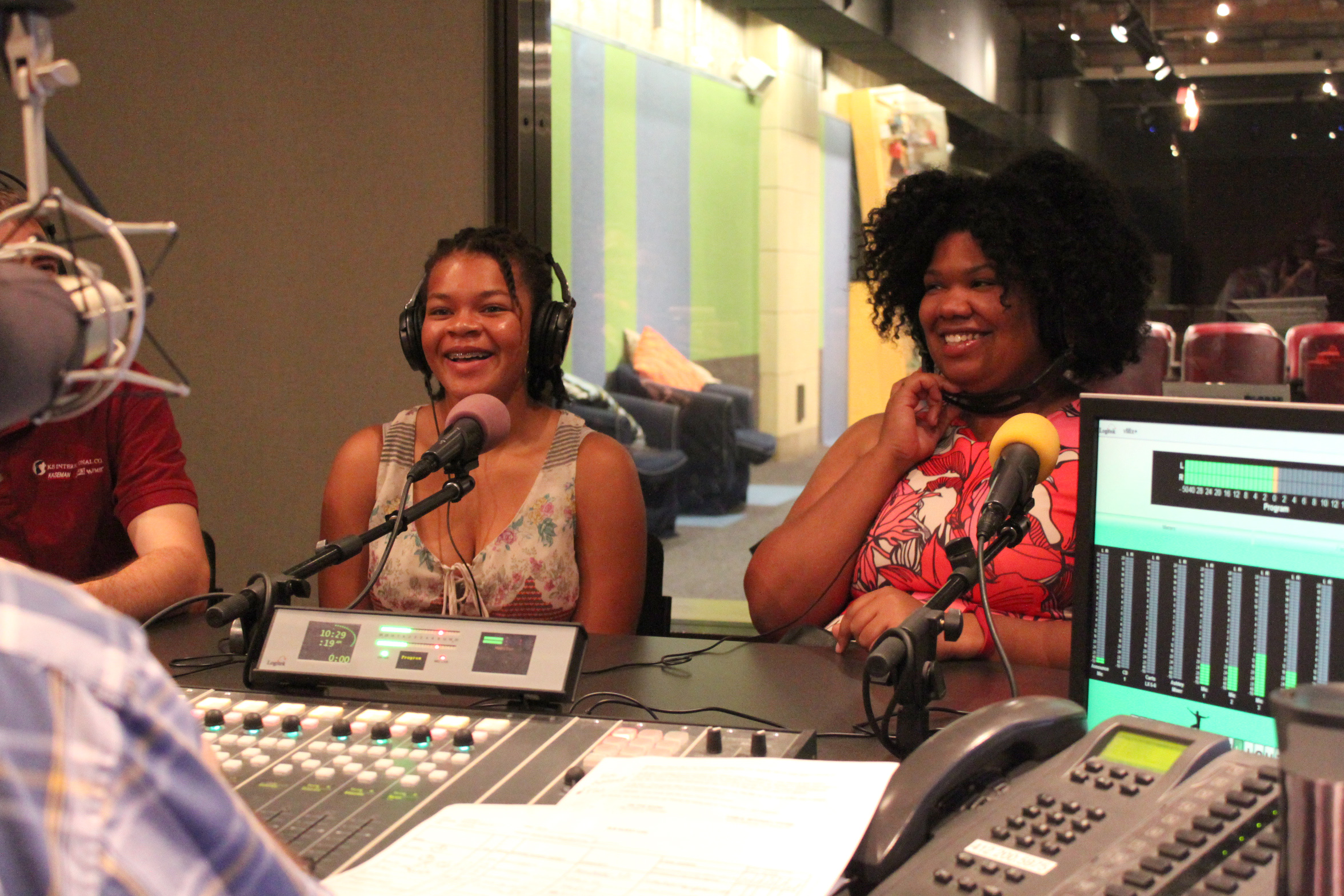 Two teens wearing headphones laughing into microphones in a radio studio