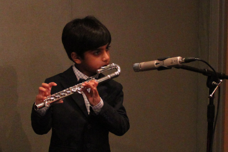 A youth playing an alto flute into a microphone in a radio studio