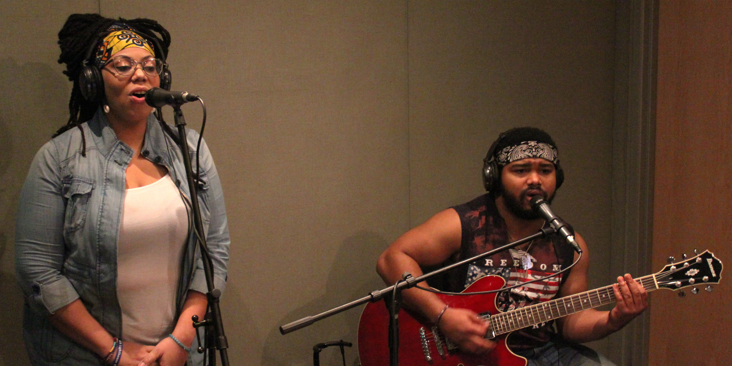 An adult singing into a microphone and an adult singing into a microphone and playing electric guitar in a radio studio
