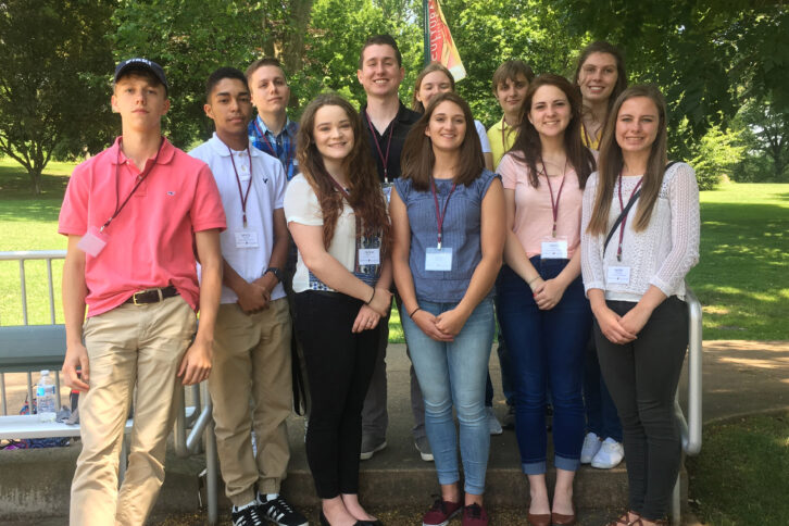 Eleven teens smiling and posing in front of a park