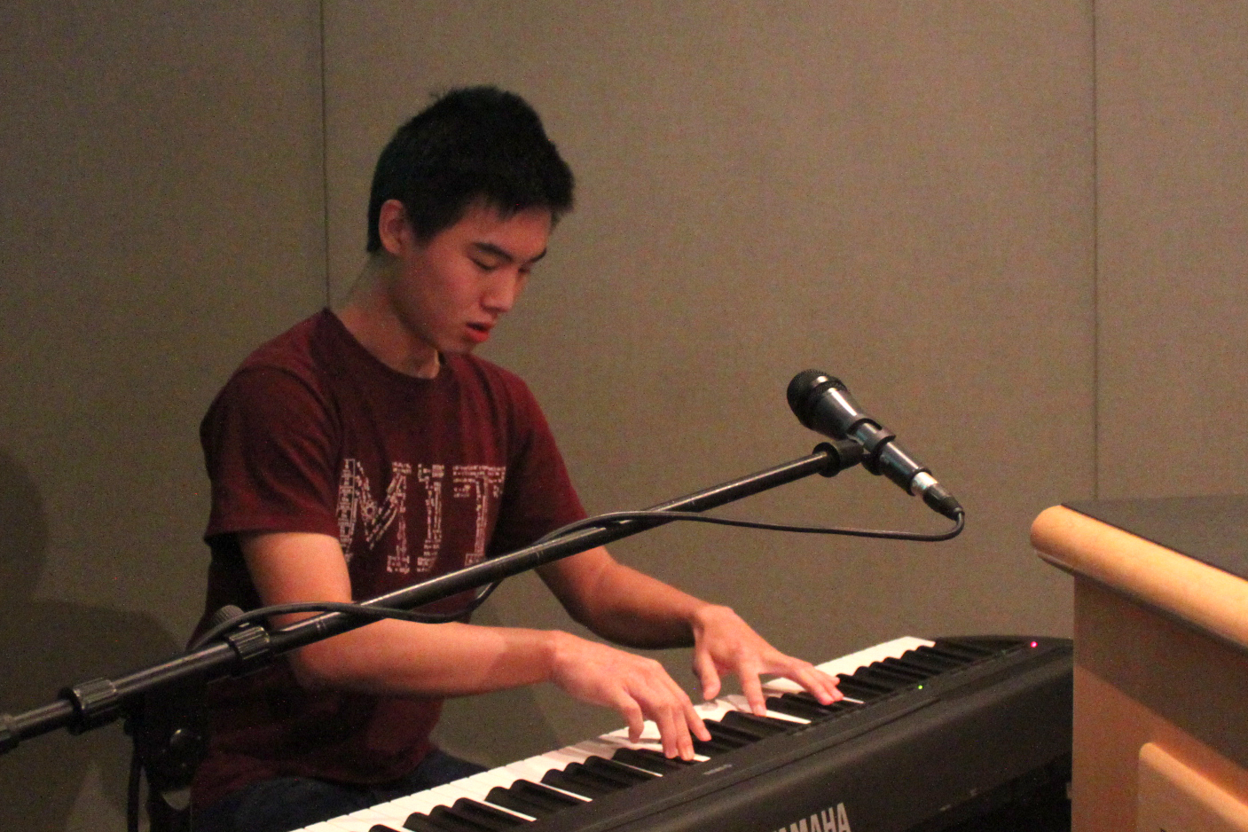 A teen playing a piano keyboard sitting behind a microphone in a radio studio