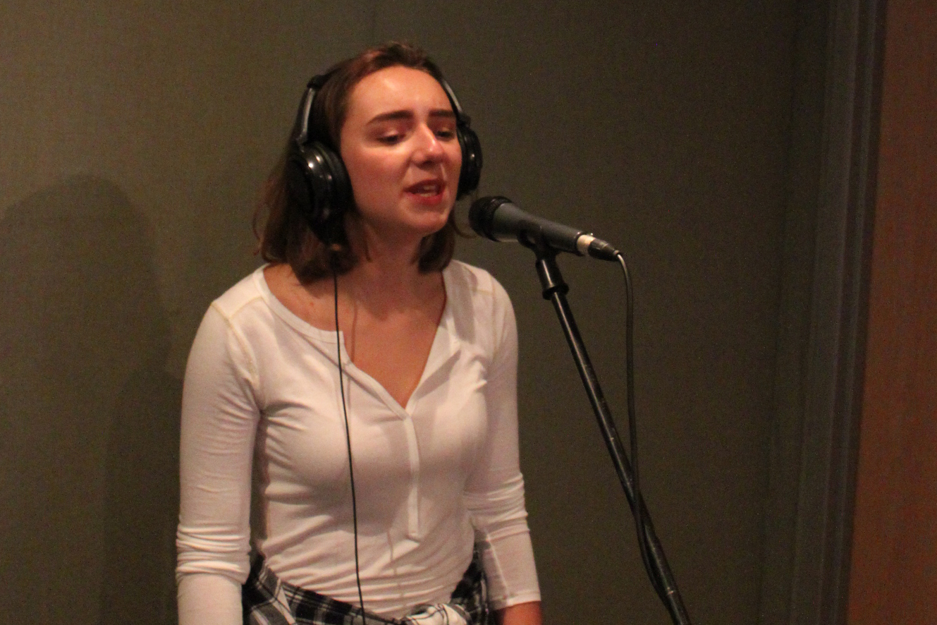 A teen wearing headphones singing into a microphone in a radio studio