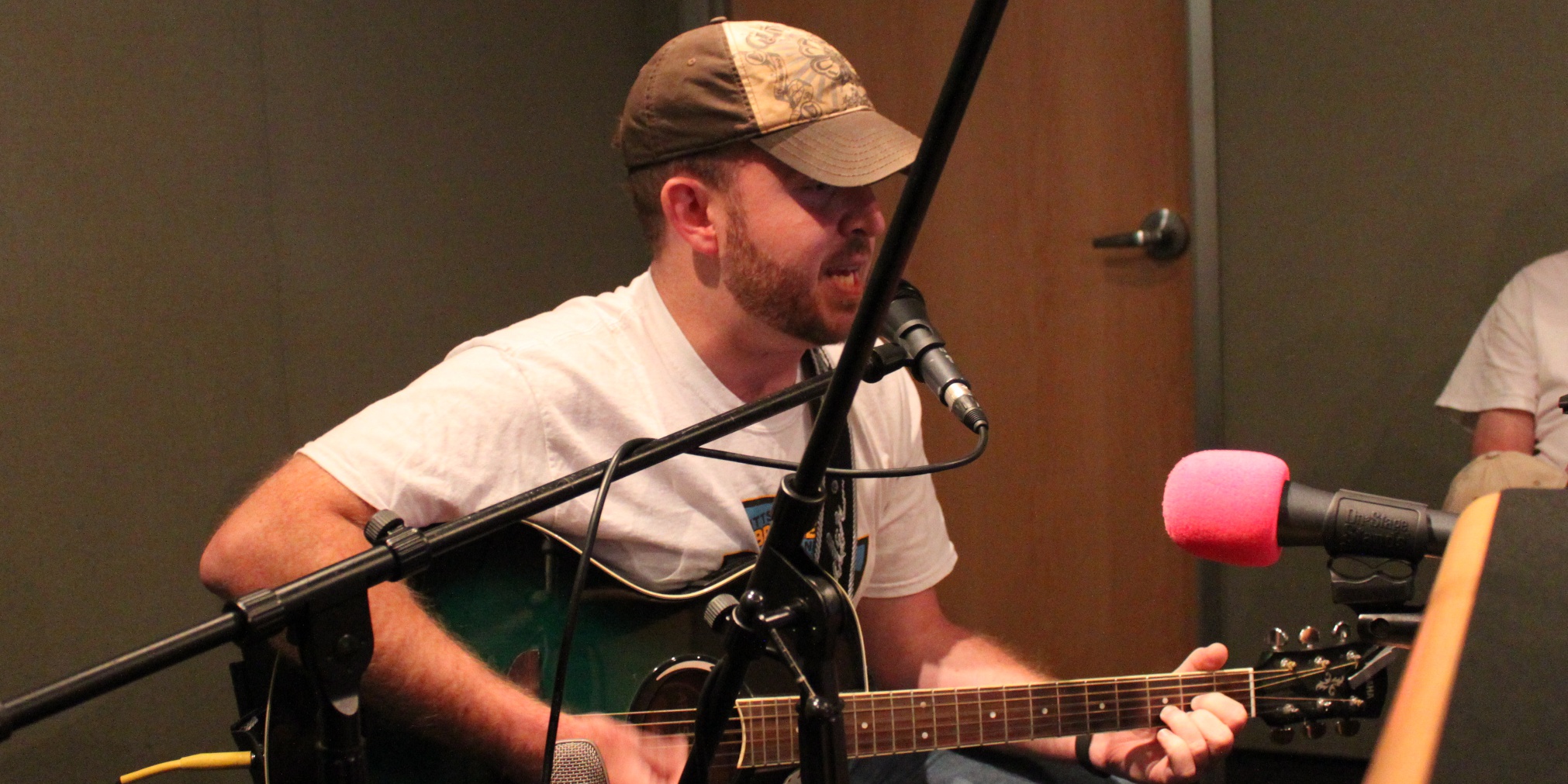 An adult singing into a microphone and playing an acoustic guitar in a radio studio