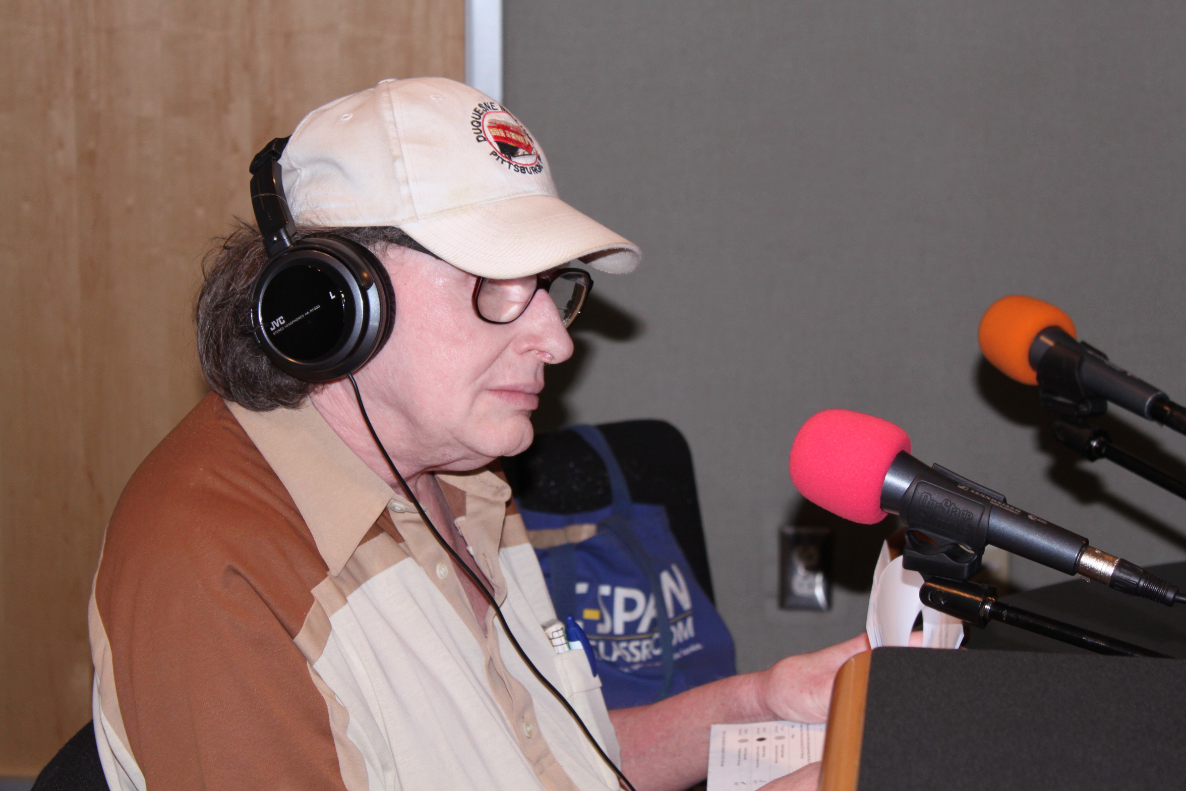 An adult wearing headphones speaking into a microphone in a radio studio