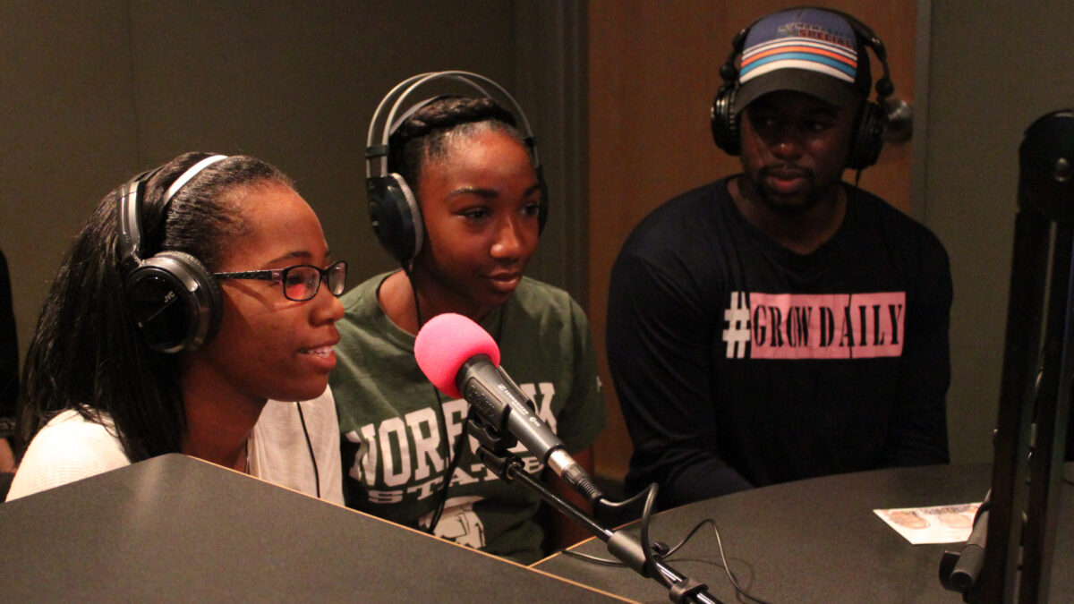 Three teens wearing headphones speaking into microphones in a radio studio