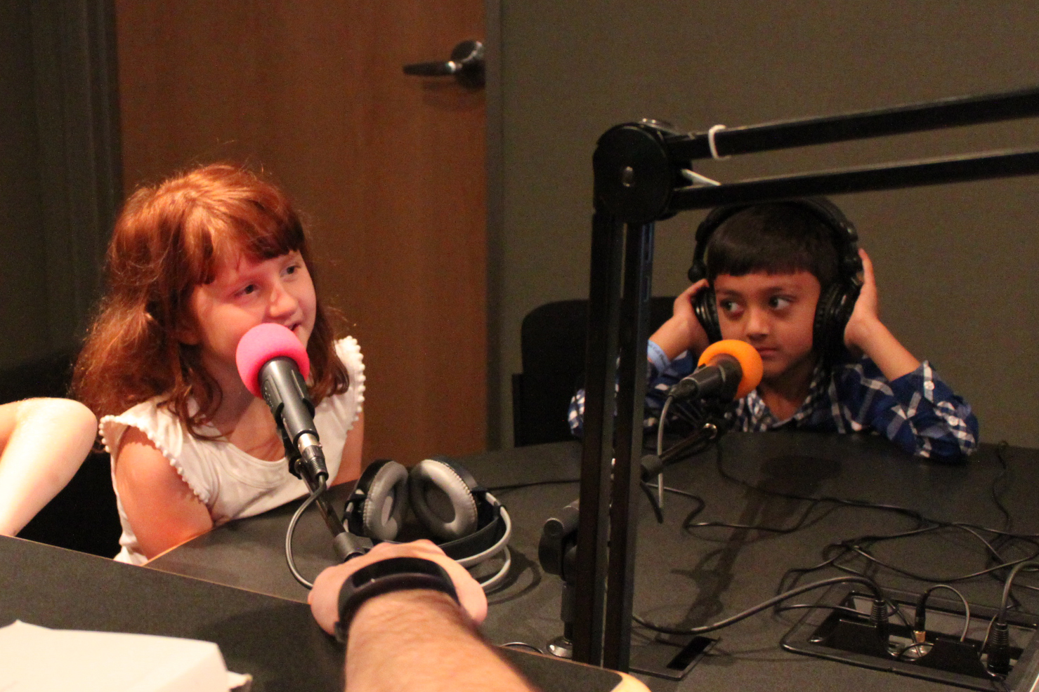 Two youth, one wearing headphones, speaking into microphones in a radio studio